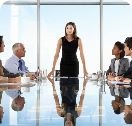 Woman standing at the front of a boardroom with seated business people.