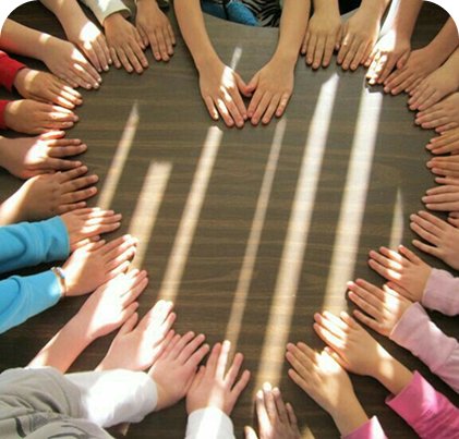 A class full of students putting their hands on a table in the shape of a heart.