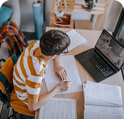 Kid working on homework while distracted by a laptop.