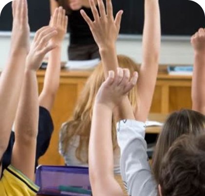 Kids in a classroom with their hands raised.