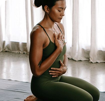 Woman in green kneeling on a yoga mat and doing yoga.