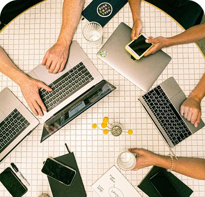 A table with several computers and people working together.