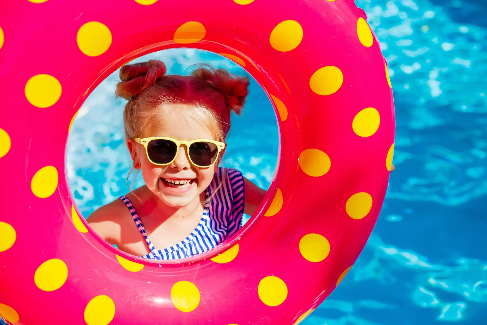 a happy little girl in sunglasses holds a swimming circle near the pool in the summer.
