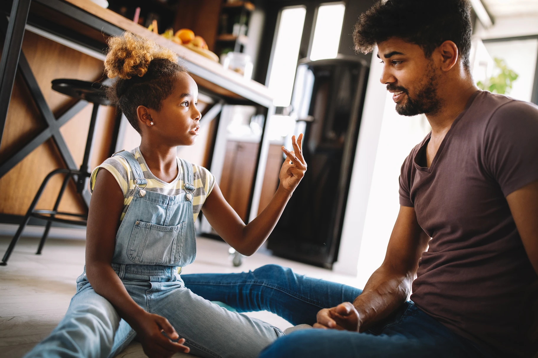 Cute african girl and her handsome father are talking and smiling at home