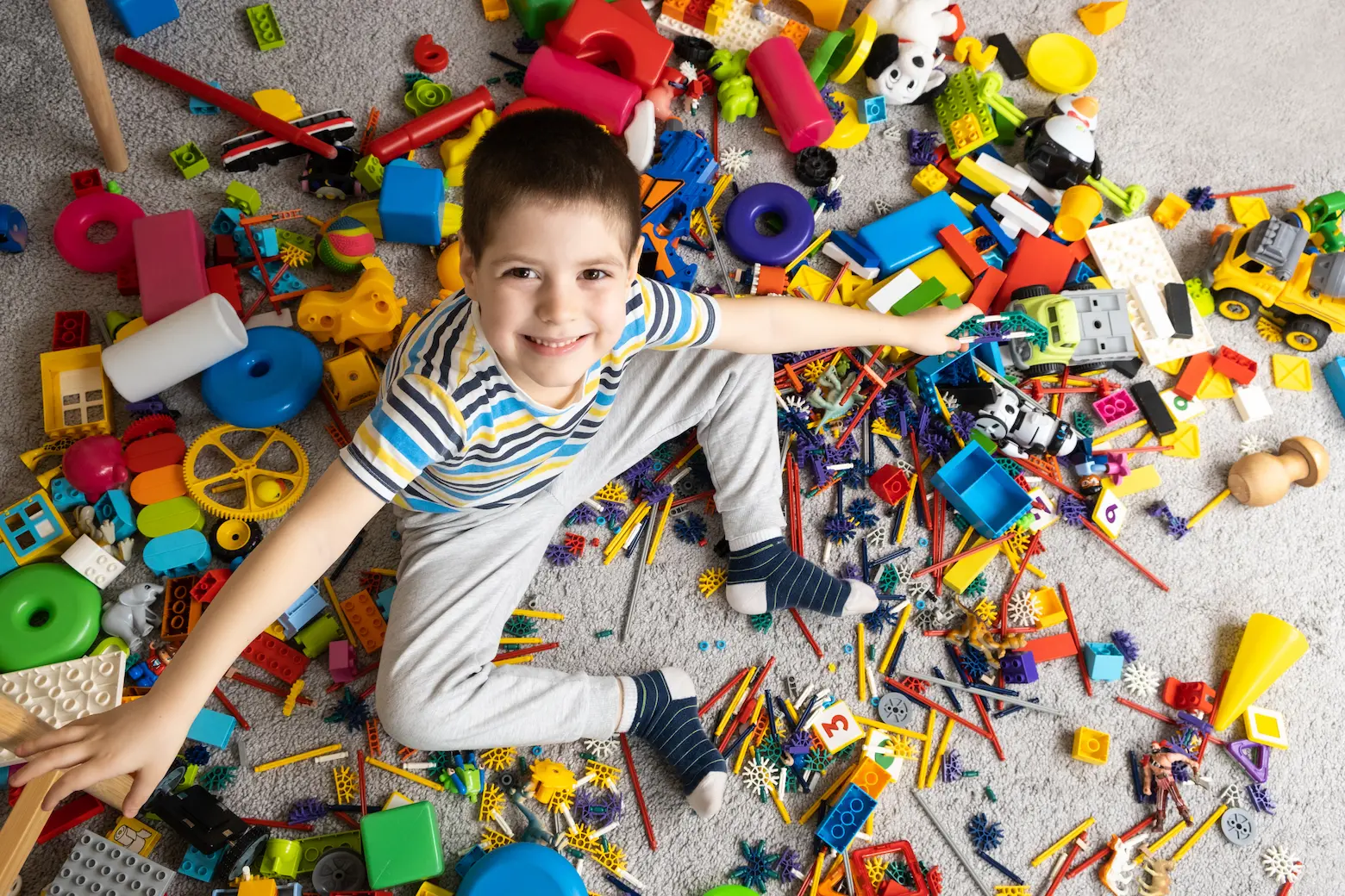 A little boy sits among scattered toys and smiles looking into the camera