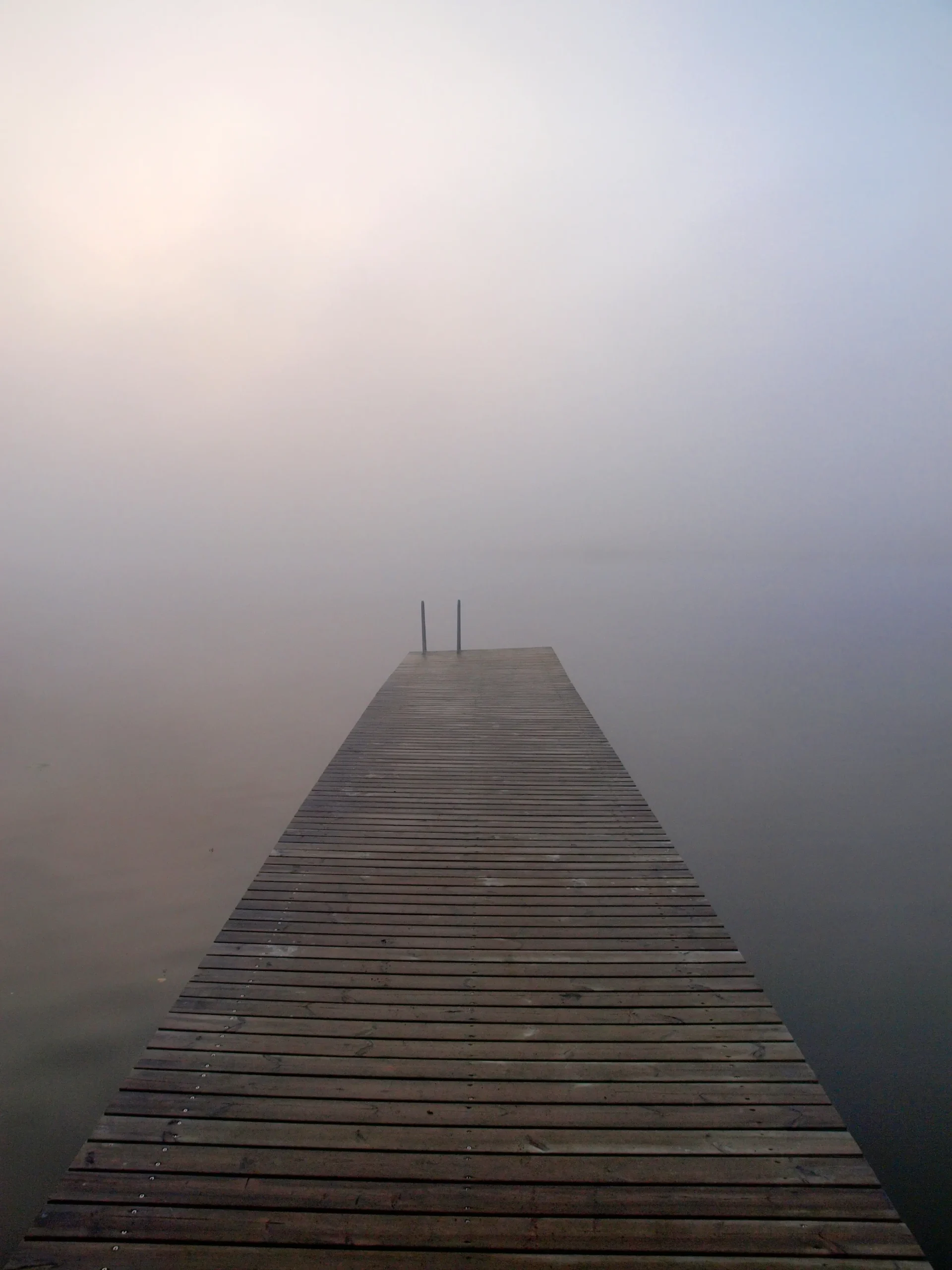 A dock on a still body of water with fog obscuring the view